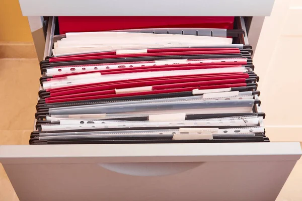 Documents organized in a metal office drawer filing cabinet full of subfolders and folders in an office