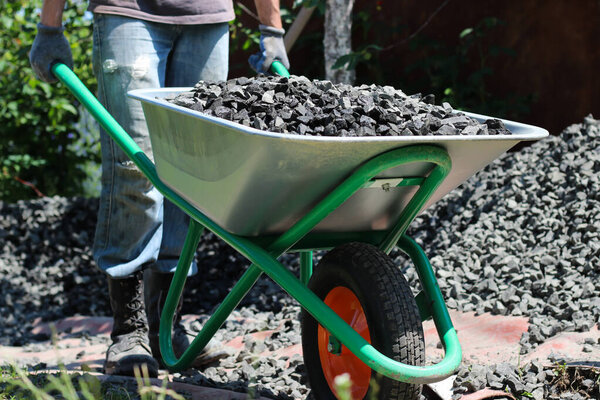 Человек за рулем тачки с дроблеными камнями, как часть строительного проекта