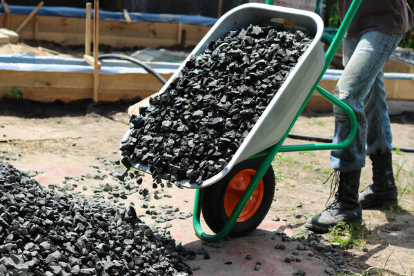 Человек двигает тачку с щебнем, как часть строительного проекта