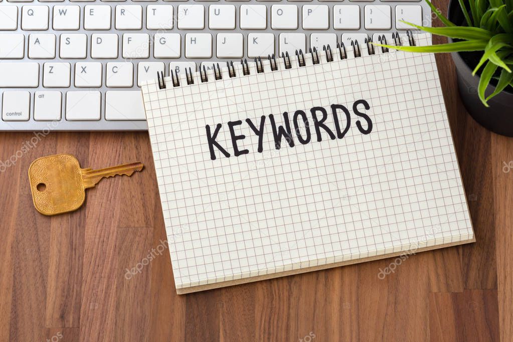 Keywords word on notebook with key and computer on wooden table