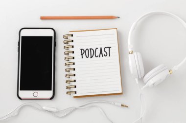 Podcast kelime defter ile akıllı telefon ve kulaklık beyaz masa, üstten görünüm