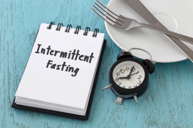 Intermittent fasting word on notepad with clock, fork and knife on white plate, intermittent fasting and weight loss  concept clipart