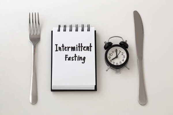 Intermittent fasting word on notepad with clock, fork and knife, weight loss plan