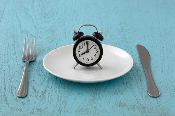 Clock on white plate with fork and knife, intermittent fasting, meal plan, weight loss concept on blue table