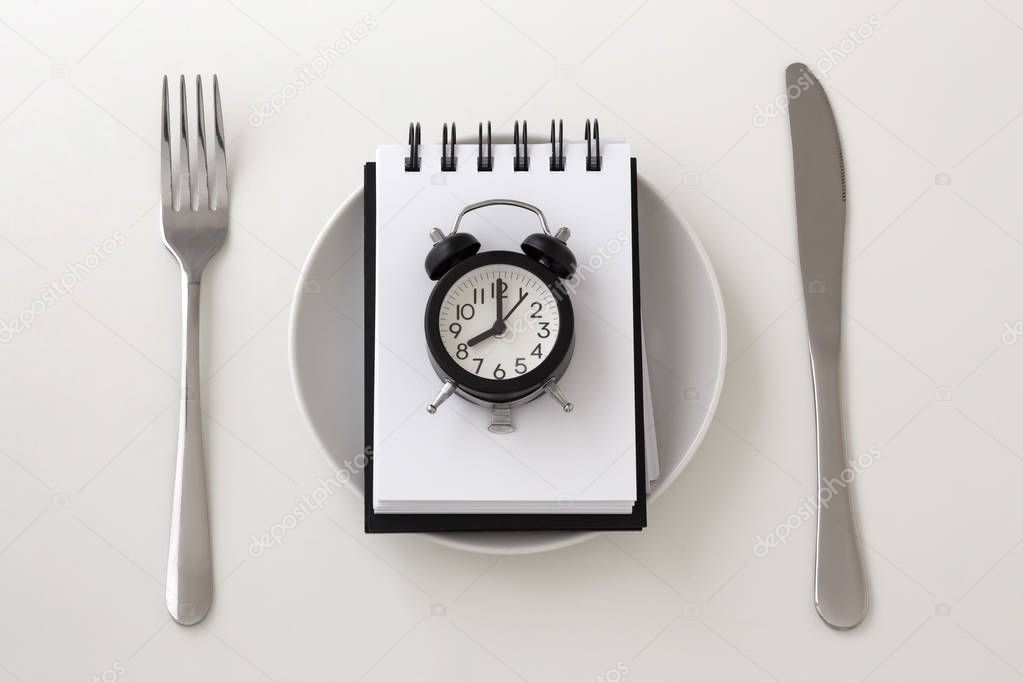 Clock on notepad with fork and knife, intermittent fasting and weight loss plan concept