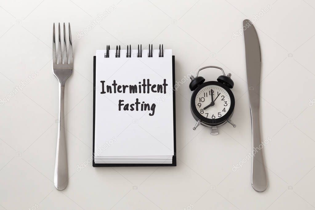 Intermittent fasting word on notepad with clock, fork and knife, weight loss plan