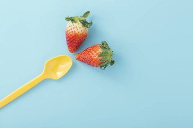 Açık mavi renkli, düz sarı kaşık ile çilek yatıyordu
