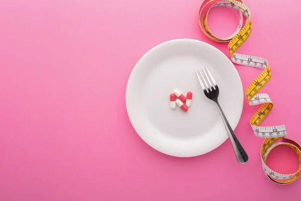 분홍색 배경의 줄자가 있는 접시 위 의식 량 보충 물 — 스톡 사진