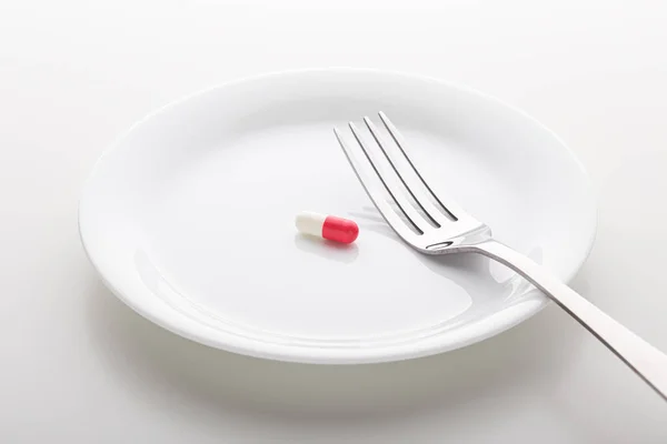 Таблетки на белой тарелке с вилкой — стоковое фото