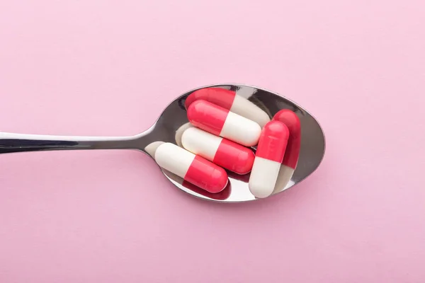 Suplemen, pil di sendok pada latar belakang merah muda — Stok Foto