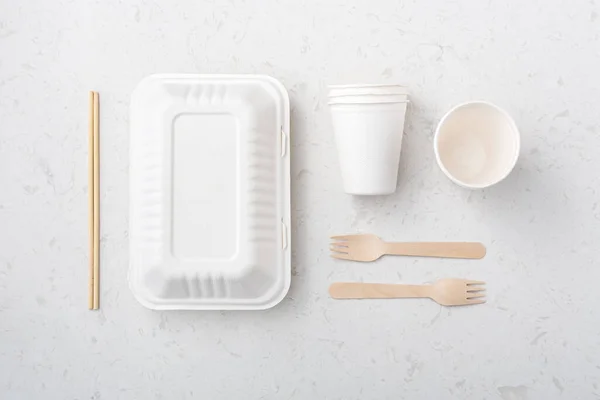 Eco friendly food packaging with box, cup, chopsticks and fork on white quartz background, flat lay