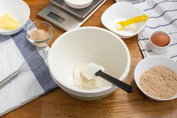 Cream cheese in mixing bowl with cookie ingredients on wooden table