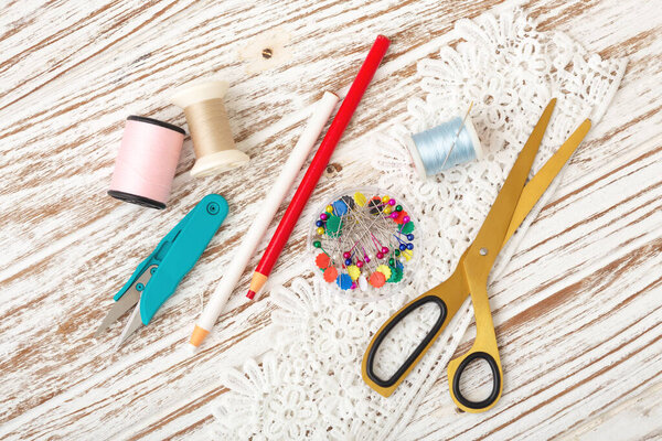 Threads and sewing accessories on white rustic wooden table, top view