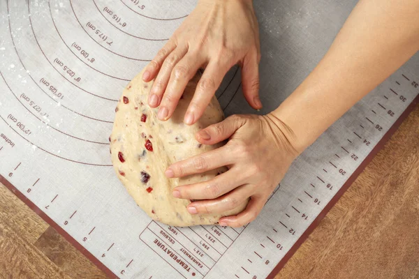 Woman hand kneading bread dough with cranberry on baking mat, top view