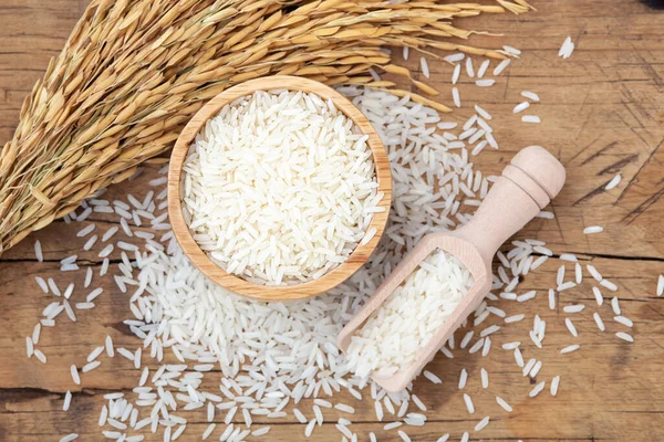 Rice in bowl with rice paddy on rustic wooden background, top view