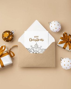 Zarfta mutlu noel kartları ve hediye kutuları ve açık kahverengi arka planda xmas topu süsü, üst görünüm, boşluğu kopyala