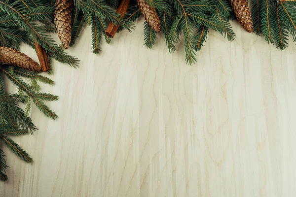 Ahşap arka planda izole edilmiş dallar, koniler ve tarçınlardan yapılmış Noel çerçevesi