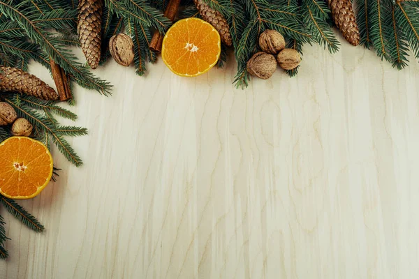 Tahta arka planda izole edilmiş dallar, koniler, cevizler, tarçın ve turunçgillerden yapılmış Noel çerçevesi