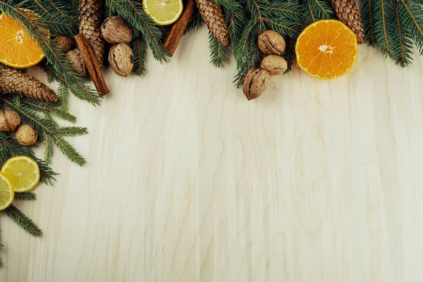 Tahta arka planda izole edilmiş dallar, koniler, cevizler, tarçın ve turunçgillerden yapılmış Noel çerçevesi