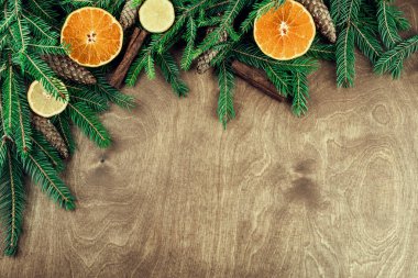 Tahta arka planda izole edilmiş dallar, koniler, cevizler, tarçın ve turunçgillerden yapılmış Noel çerçevesi
