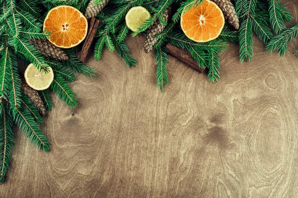 Tahta arka planda izole edilmiş dallar, koniler, cevizler, tarçın ve turunçgillerden yapılmış Noel çerçevesi