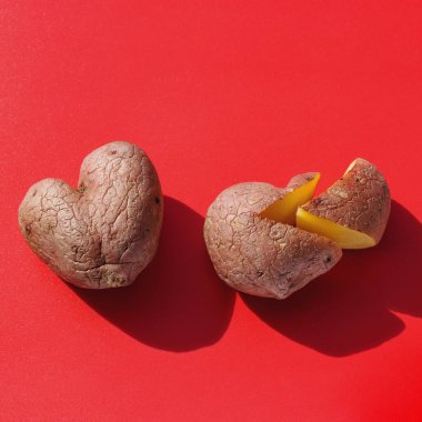 Kırmızı zemin üzerinde kalp şeklinde iki çiğ patates, bir patates dilimlenir. Kare fotoğraf biçimi. Patates aşk hikayesi. Kopya alanı, kırık kalp kavramı, aşk testi, aile hayatı, aşk fedakarlığı, çirkin sebzeler.