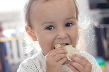 Küçük kıvırcık kız krep yer. Yakın plan, seçici odaklanma. Küçük bir çocuk iştah açıcı bir şekilde ev yapımı krep yer. Sağlıklı çocuk kahvaltısı. Sağlıklı ürünlerden un ürünleri.