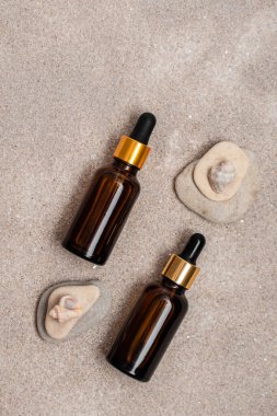 Cilt bakımı için pipeti olan cam kahverengi serum şişeleri kum üzerinde taş ve deniz kabuklarıyla birlikte. Deniz bileşenli kozmetik ürünleri. Sağlık ve güzellik kavramı. minimalizm, boşluğu kopyala
