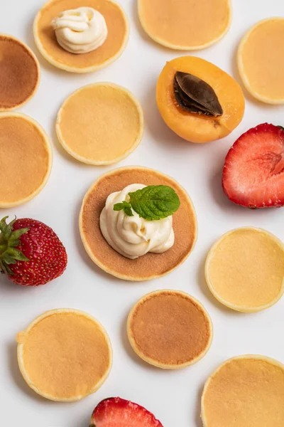 Das Muster aus kleinen Pfannkuchen, frischen Erdbeeren und Aprikosen ist komplett ausgelegt. Hintergrund sind orangefarbene Toasts rund um Pfannkuchen. Trendfood — Stockfoto