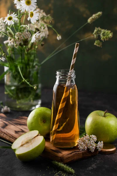 Yeşil elma ve kır çiçekleriyle dolu cam bir şişede elma suyu ile kompozisyon. Detoks, diyet, temiz yemek, vejetaryen, vegan, fitness veya sağlıklı yaşam tarzı konsepti.