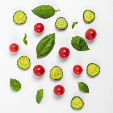 Domates, salatalık ve fesleğen yapraklarının yaratıcı bir kopyası. Düz yerde, üst tarafta. Yemek konsepti. Beyaz arka planda izole edilmiş sebzeler.