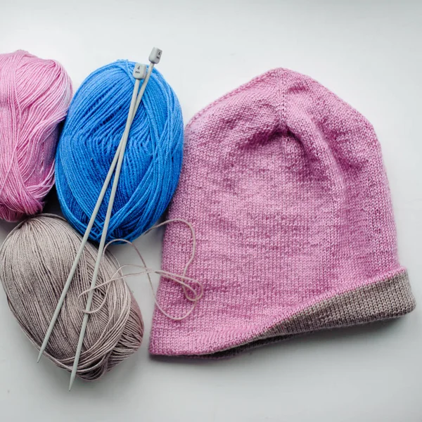 Çok renkli yün iplikler örgü iğneleri ve açık arkaplanda örülmüş bir şapka. Alpaca, merino ipliği. Örgü ve örgü örmek için iplikler. Yaratıcılık ve hobiler.