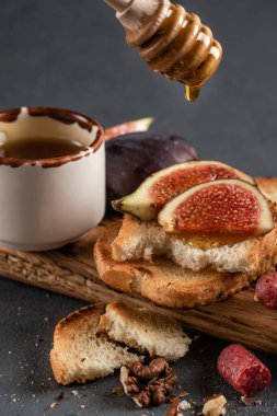 Tahtaya yakın planda incirli çıtır tost ve bal. Karanlık bir taşta romantik bir randevu için yemek. Kopyalama alanı olan üst görünüm, koyu arkaplan.