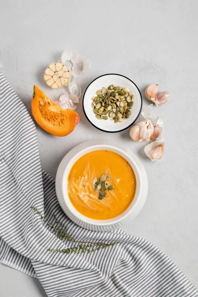 A bowl of pumpkin cream kabocha soup, garnished with pumpkin seeds, served with cream. High angle view, gray concrete background. Healthly food. — Stock Photo, Image