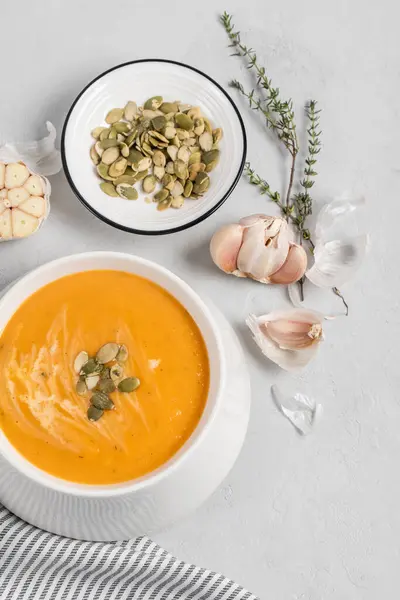 A bowl of pumpkin cream kabocha soup, garnished with pumpkin seeds, served with cream. High angle view, gray concrete background. Healthly food. — Stock Photo, Image