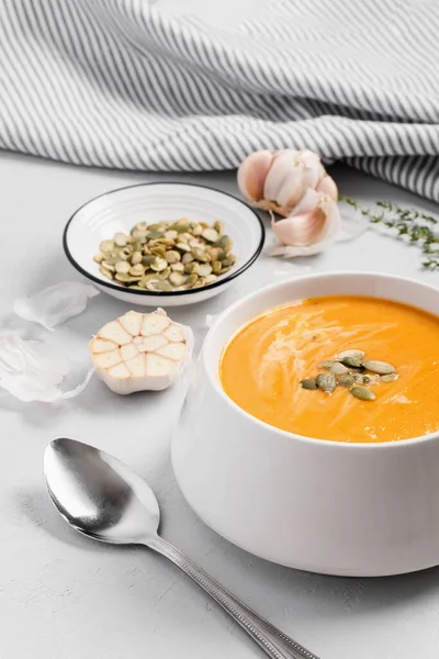 A bowl of pumpkin cream kabocha soup, garnished with pumpkin seeds, served with cream. Close-up, gray concrete background. Healthly food — Stock Photo, Image