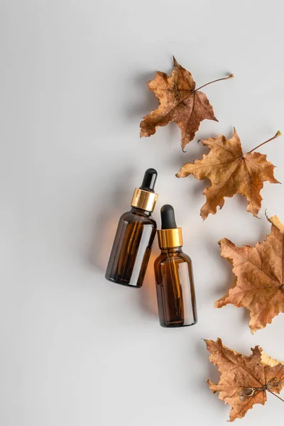 Sonbahar yapraklı, beyaz arka planda deri bakım pipeti olan cam kahverengi serum şişeleri. Sağlık ve güzellik konsepti. minimalizm, üst görünüm