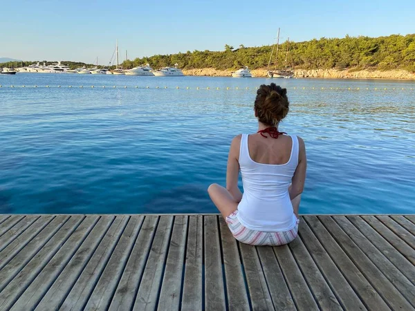 Denizde ahşap zeminde oturan kadın 