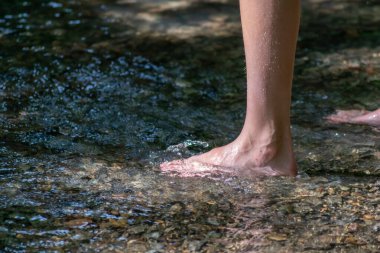 Küçük bir derede çıplak ayakla temiz suyla oynayan genç bir çocuk ayaklarını ve su kaynağını kullanarak ayak parmaklarını ve bacaklarını serinletiyor ve zen meditasyon atmosferindeki saf yaşam iksiriyle ferahlatıyor.