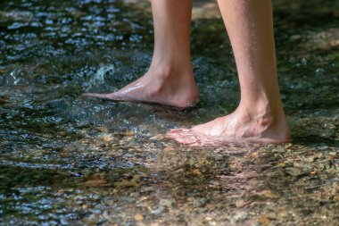 Küçük bir derede çıplak ayakla temiz suyla oynayan genç bir çocuk ayaklarını ve su kaynağını kullanarak ayak parmaklarını ve bacaklarını serinletiyor ve zen meditasyon atmosferindeki saf yaşam iksiriyle ferahlatıyor.