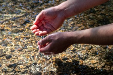 Avrupalı bir erkek el, ferahlatıcı bir zen atmosferde kristal gibi berrak bir suyun içinde ipeksi dalgalar ve yüzen dalgalar ve suda taş arayan güneşli yansımalarla.
