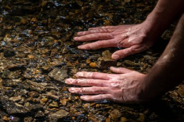 Avrupalı bir erkek el, ferahlatıcı bir zen atmosferde kristal gibi berrak bir suyun içinde ipeksi dalgalar ve yüzen dalgalar ve suda taş arayan güneşli yansımalarla.