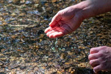 Avrupalı bir erkek el, ferahlatıcı bir zen atmosferde kristal gibi berrak bir suyun içinde ipeksi dalgalar ve yüzen dalgalar ve suda taş arayan güneşli yansımalarla.