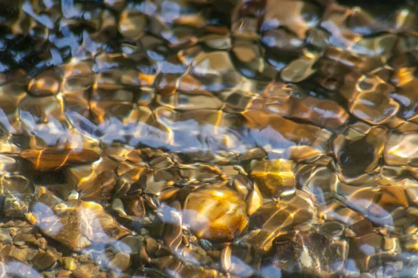 Stones in sparkling water with sunny reflections in water of a crystal clear water creek as idyllic natural background shows zen meditation, little waves and silky ripples in a healthy mountain spring