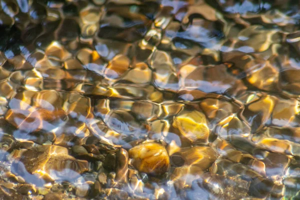 Stones in sparkling water with sunny reflections in water of a crystal clear water creek as idyllic natural background shows zen meditation, little waves and silky ripples in a healthy mountain spring