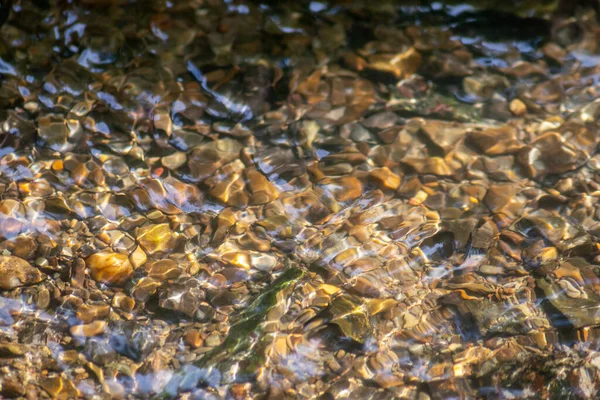 Stones in sparkling water with sunny reflections in water of a crystal clear water creek as idyllic natural background shows zen meditation, little waves and silky ripples in a healthy mountain spring