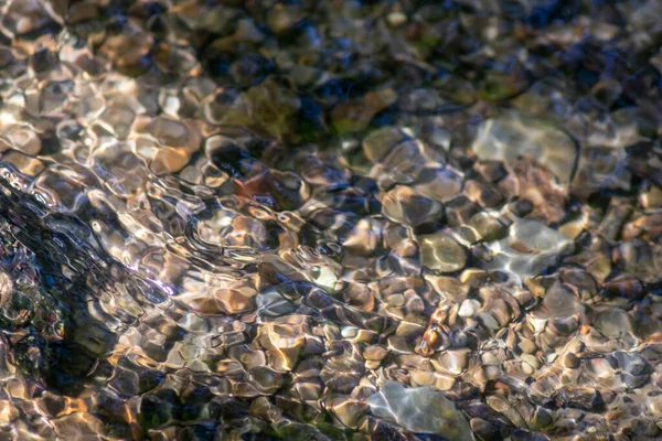 Stones in sparkling water with sunny reflections in water of a crystal clear water creek as idyllic natural background shows zen meditation, little waves and silky ripples in a healthy mountain spring