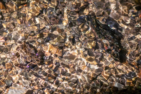 Stones in sparkling water with sunny reflections in water of a crystal clear water creek as idyllic natural background shows zen meditation, little waves and silky ripples in a healthy mountain spring