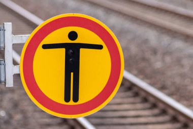 Bulanık arka planda tren istasyonuna izinsiz giriş işareti yok. Yolcu ve misafirlere zarar gelmesin diye turuncu tabelanın üzerinde kırmızı halkalı siyah bir insan sembolü görülüyor.
