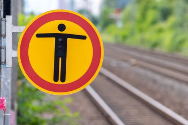 Bulanık arka planda tren istasyonuna izinsiz giriş işareti yok. Yolcu ve misafirlere zarar gelmesin diye turuncu tabelanın üzerinde kırmızı halkalı siyah bir insan sembolü görülüyor.